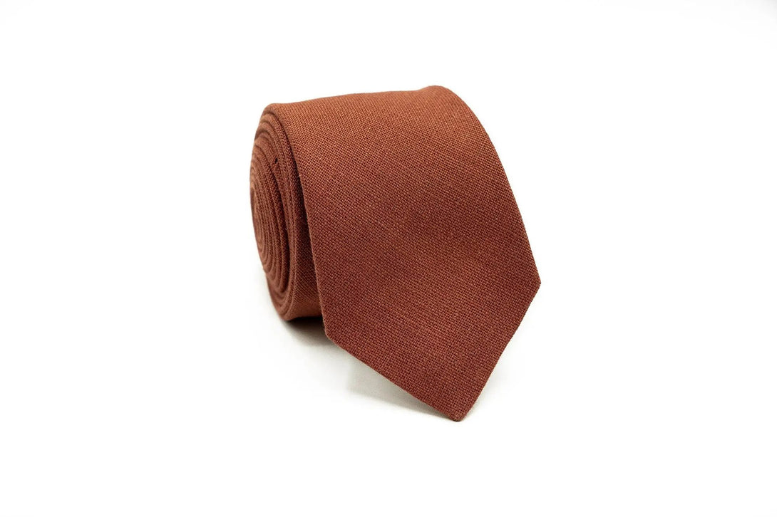 Rust linen necktie for men – A classic rust-colored linen necktie rolled neatly, suitable for weddings, groomsmen gifts, and formal attire.