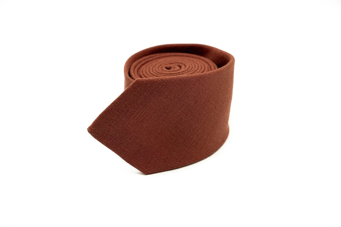 Rust linen necktie rolled neatly, showcasing its textured fabric