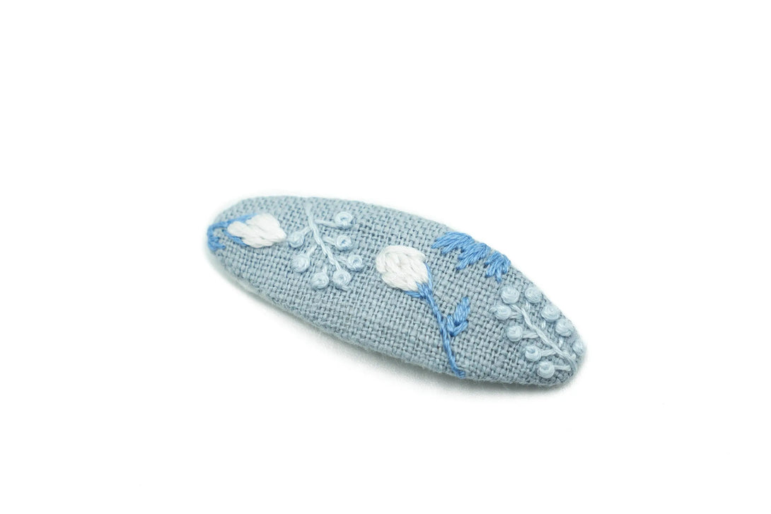 Elegant dusty blue floral hand-embroidered hair clip, perfect for wedding parties, featuring intricate white and blue flower details, eco-friendly packaging by UrbaVana.