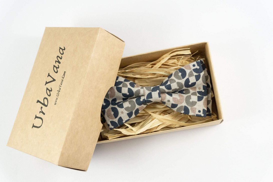 Stylish pre-tied bow tie with beige, black, and brown geometric pattern, presented in an elegant kraft paper box with 'Urbanova' branding, nestled on decorative straw, perfect for adding retro charm to disco and dance events